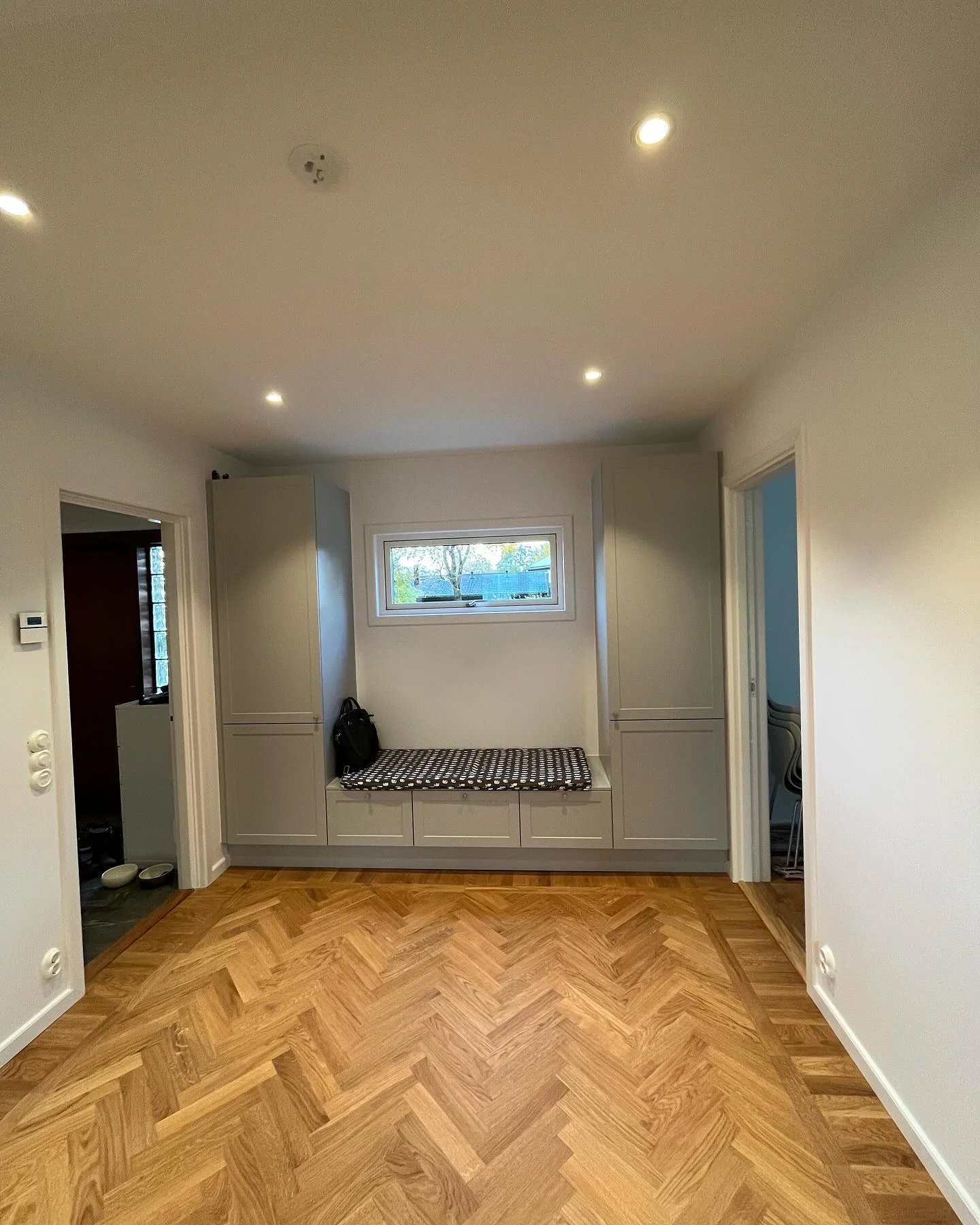 Ljus hall med parkettgolv, inbyggd bänk och garderober.