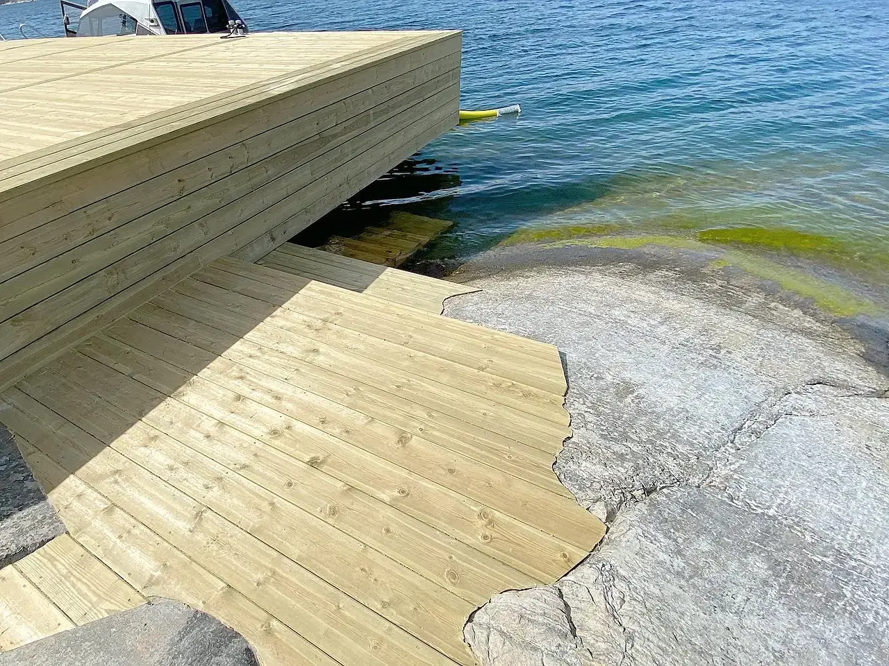 Träbrygga med trappa som leder ner till klippor vid vatten.