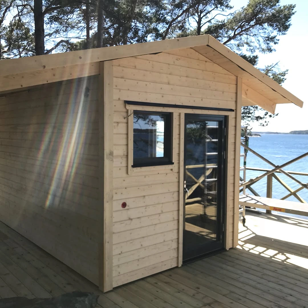 Ljust trähus med glasdörr på terrass vid havet.