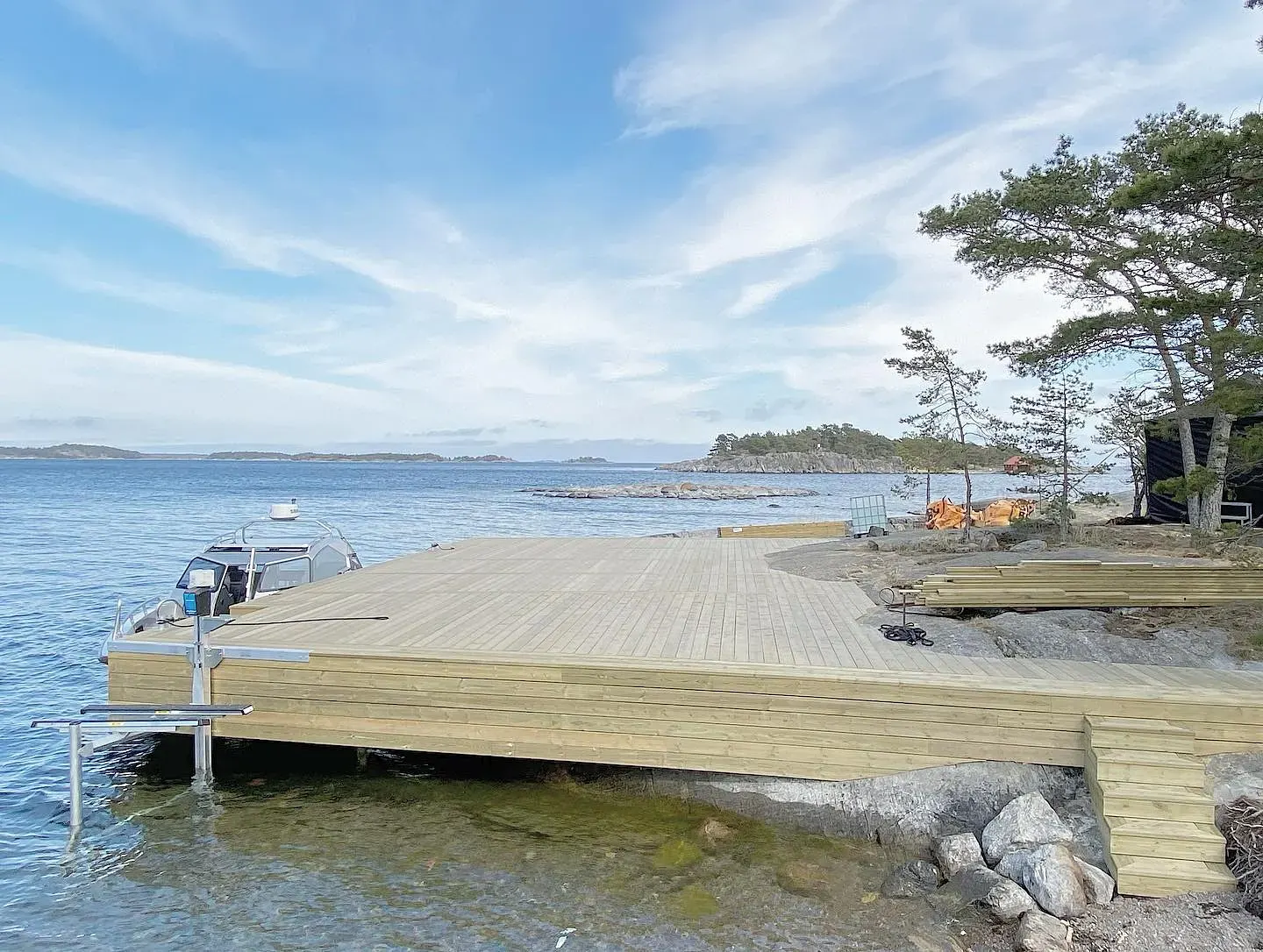 Brygga av trä vid skärgårdskust med båt och träd