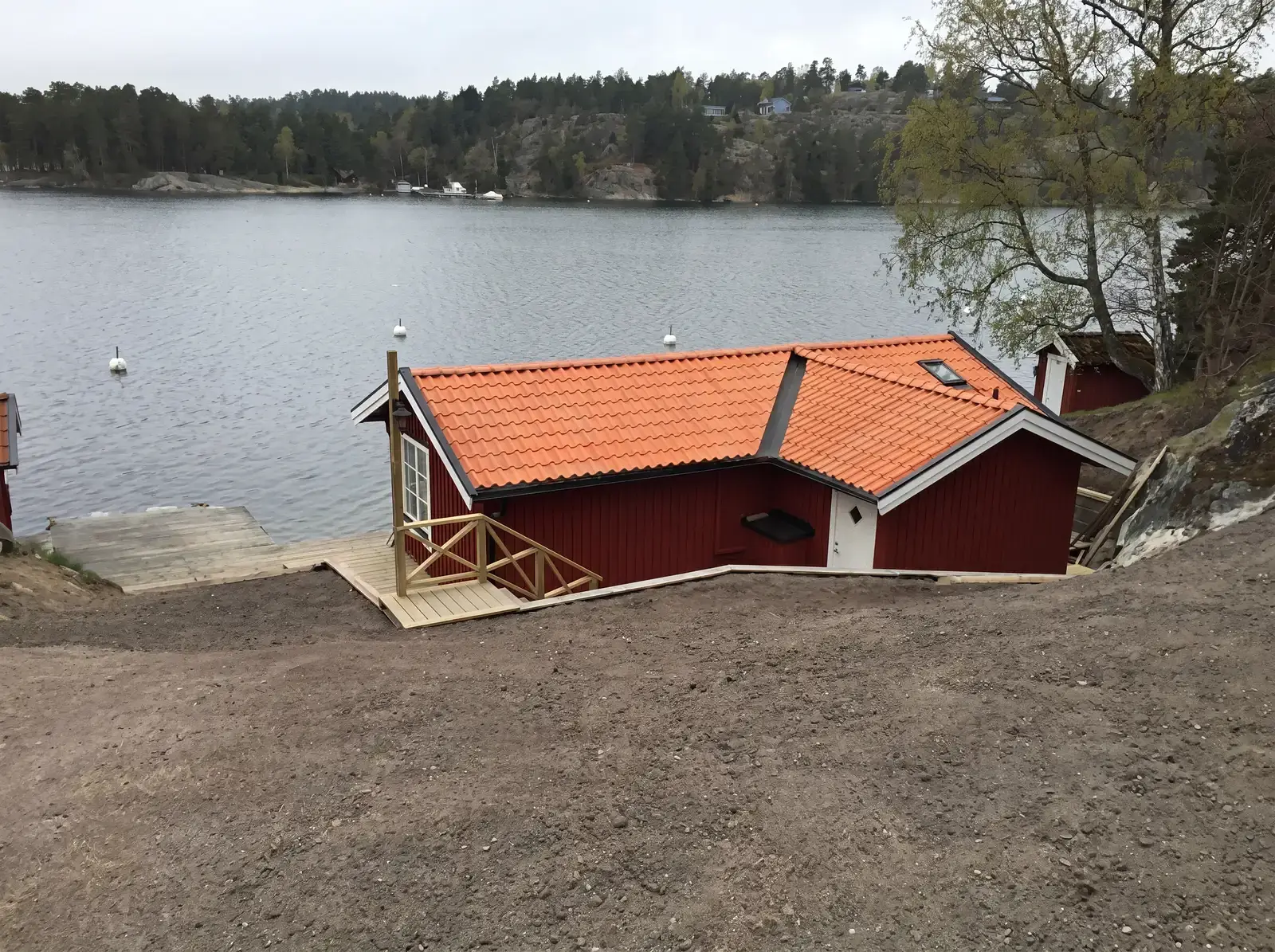 Rött sjöbod med orange takpannor vid vattnet med brygga.