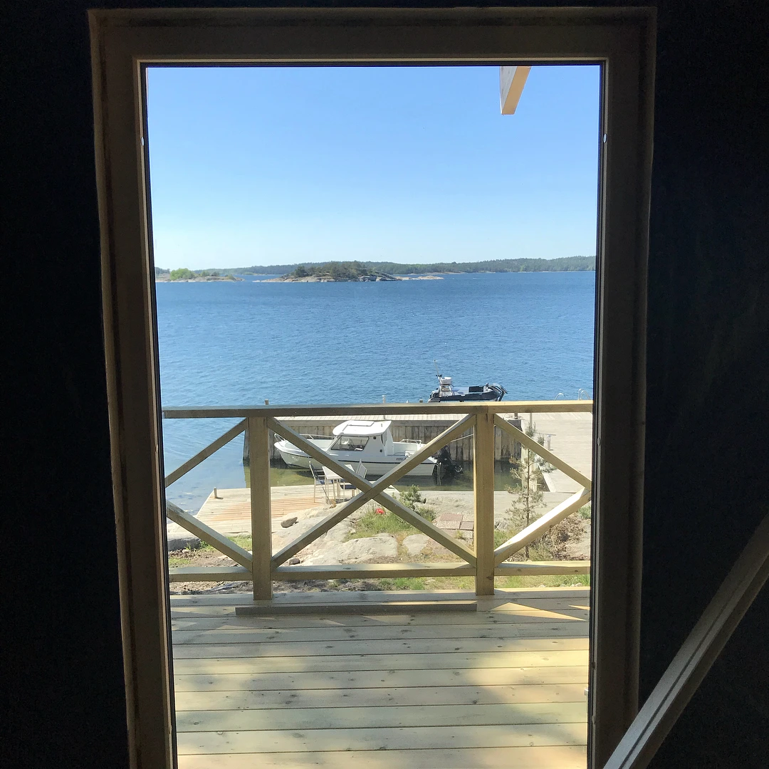 Utsikt genom dörröppning mot hav, brygga och båtar genom träräcke.